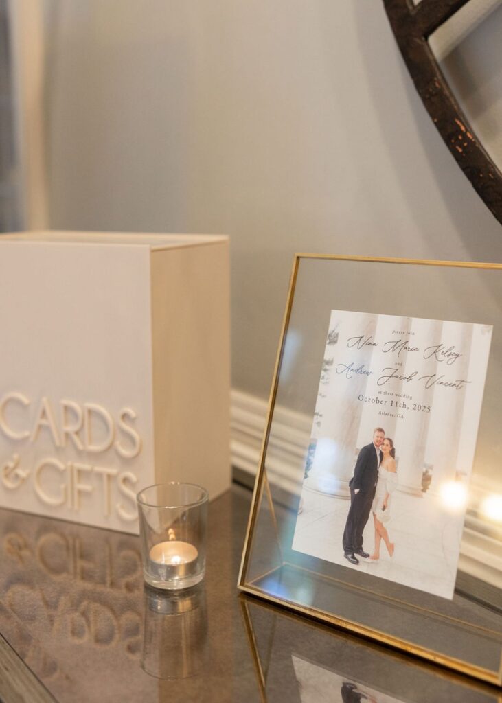 A wedding display at a Chastain Horse Park wedding reception features a Cards & Gifts box, a small lit candle in a glass holder, and a framed photo of the couple with wedding details, including the date October 13th, 2023.