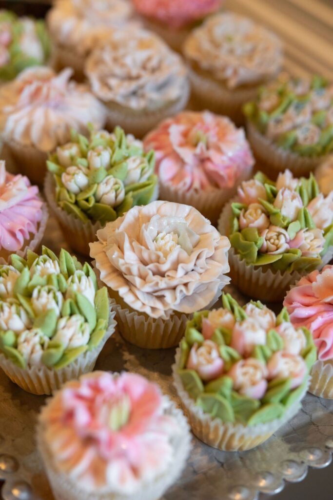 Cupcakes decorated with intricate buttercream flowers in soft pastel colors, including pink, white, and green, arranged closely together on a tray—perfect for a Chastain Horse Park wedding reception.