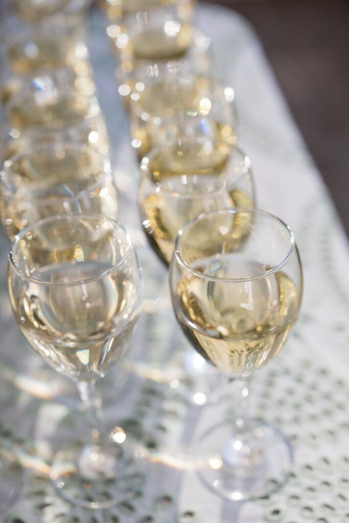 Several glasses of white wine are arranged in neat rows on a white patterned surface, reflecting light and creating a festive atmosphere.