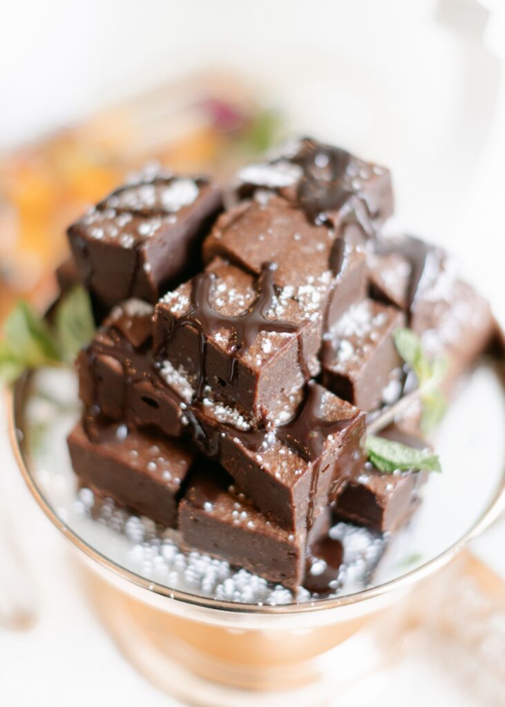 A stack of chocolate fudge squares drizzled with chocolate sauce and sprinkled with powdered sugar, garnished with fresh mint leaves—perfect for a progressive cocktail reception in Atlanta, served elegantly on a glass cake stand.