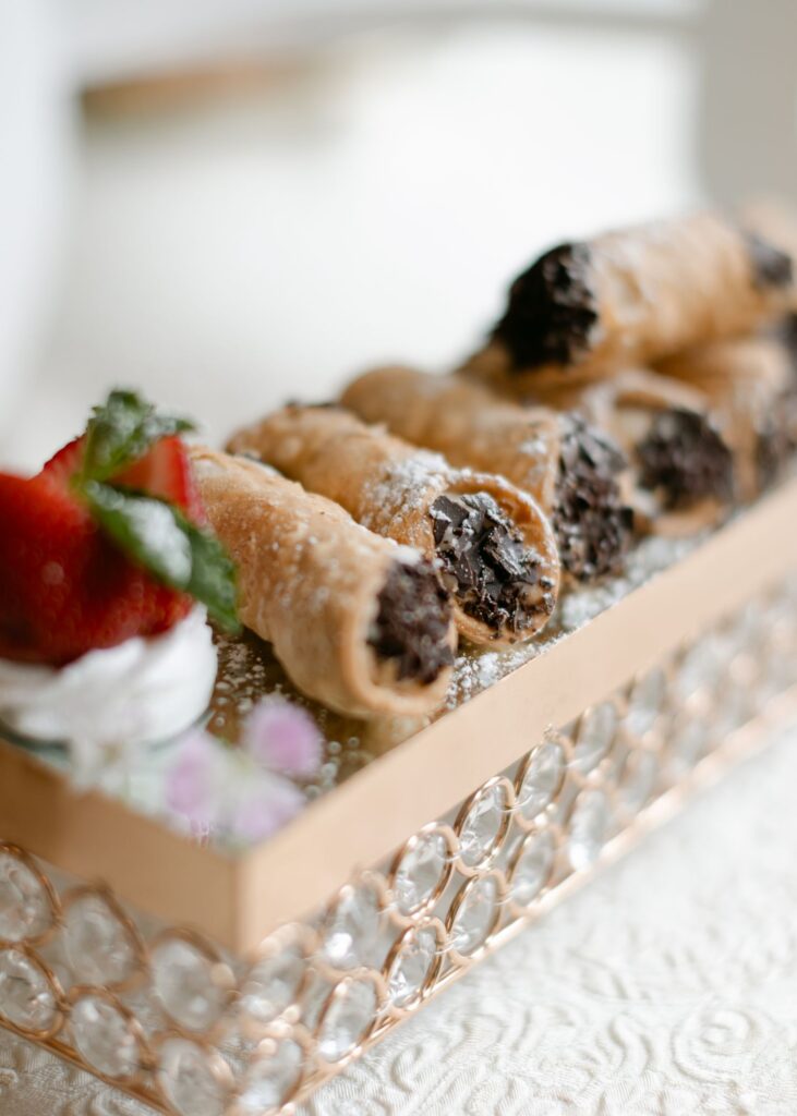 A row of chocolate-filled cannoli dusted with powdered sugar, garnished with strawberry and mint, served on a crystal-trimmed tray—an elegant dessert perfect for a progressive cocktail reception in Atlanta.