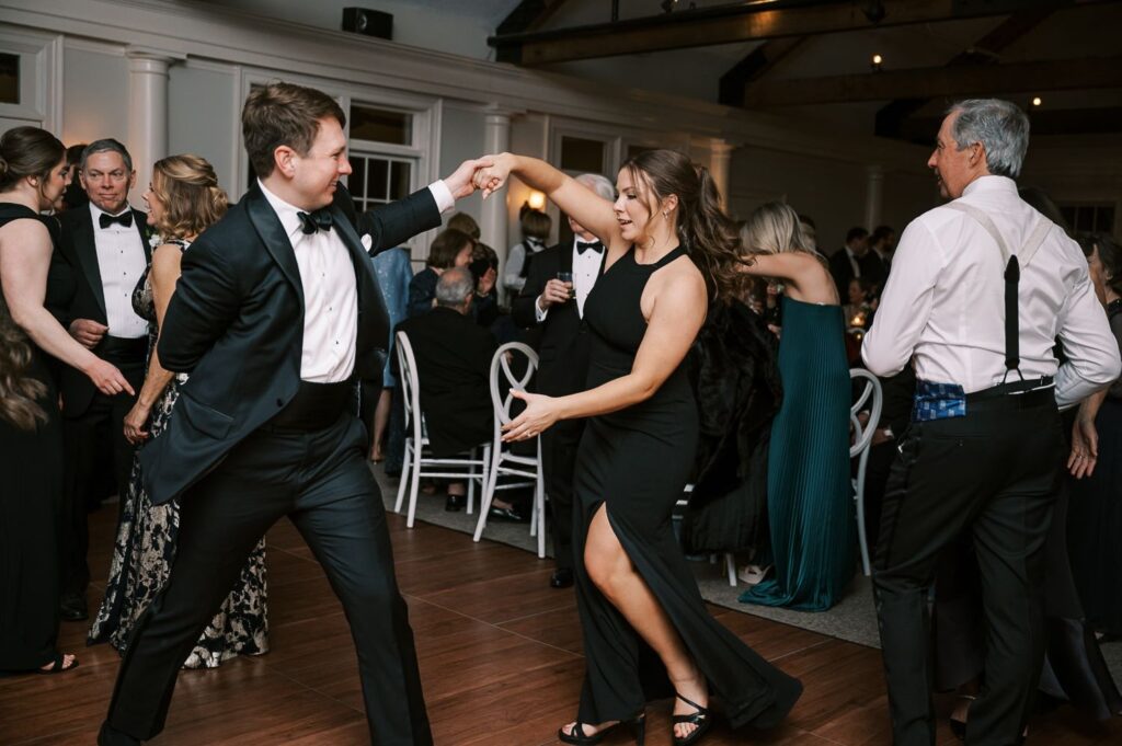 A man and woman in formal attire dance energetically at a progressive buffet wedding in Atlanta, surrounded by guests in evening wear. The atmosphere is lively, with everyone mingling and enjoying the festive occasion.