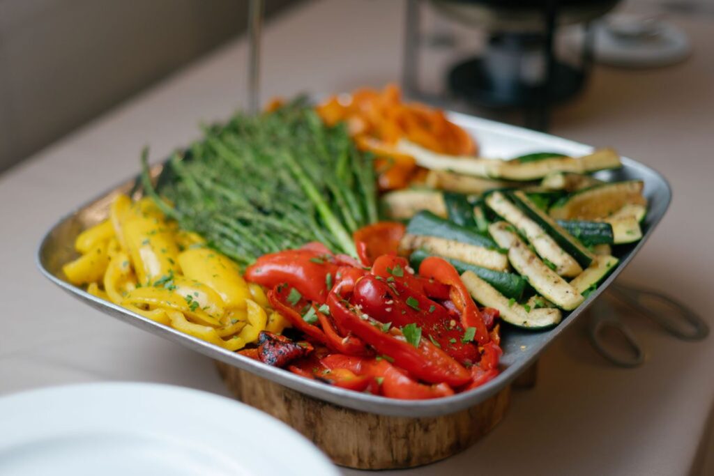 A tray of assorted grilled vegetables, including yellow and red bell peppers, asparagus, zucchini, and carrots, garnished with chopped herbs and served on a wooden stand—perfect for your Chastain Horse Park rehearsal dinner.