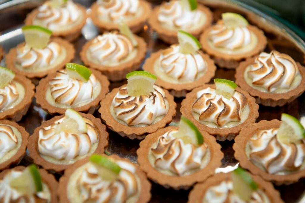 Mini tartlets with toasted meringue swirls, each topped with a small slice of lime, are arranged closely together on a reflective tray—perfect for serving at engagement party venues in Atlanta.