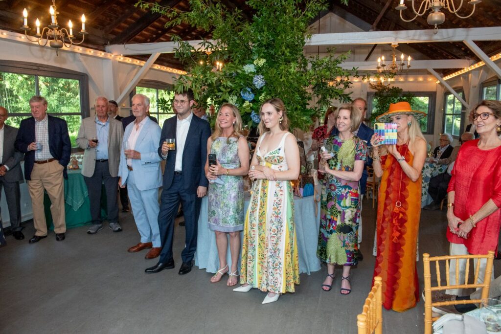 A group of people in colorful, semi-formal attire stand indoors at an event, smiling and holding drinks, with greenery and string lights in the background—capturing the festive ambiance often found at top engagement party venues Atlanta has to offer.