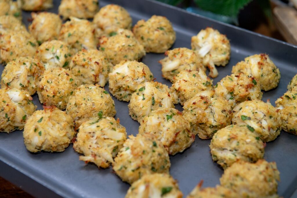 A tray filled with rows of golden-brown crab cake balls, sprinkled with chopped herbs and flaky pieces of crab meat, ready to be served—a perfect appetizer choice for celebrations at top engagement party venues Atlanta has to offer.