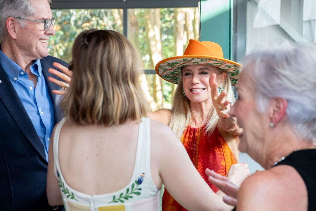 A smiling woman in an orange hat reaches out to hug another woman in a white dress, while two other people stand nearby, all appearing happy and engaged in conversation—capturing the joyful atmosphere often found at the best engagement party venues Atlanta has to offer.