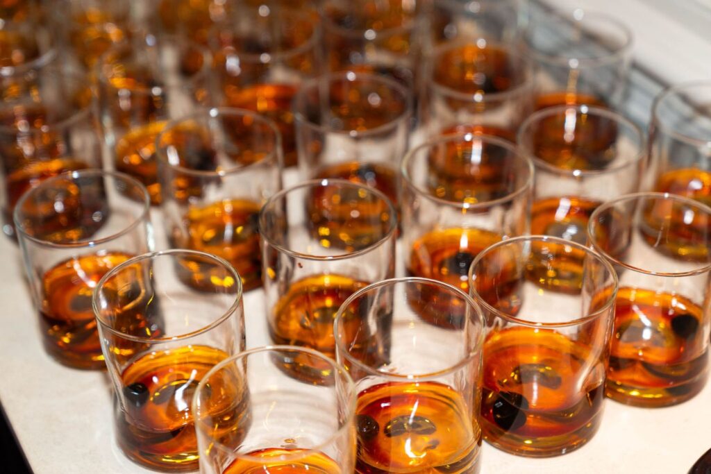 Dozens of clear glasses filled with amber-colored liquid, possibly whiskey or bourbon, are arranged closely together on a light surface—evoking the sophisticated atmosphere often found at wedding venues Atlanta couples choose for their celebrations.