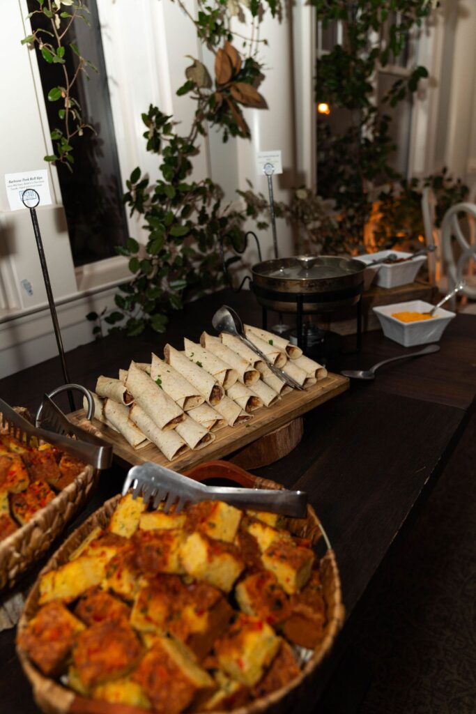 A buffet table with baskets of baked savory squares and a platter of rolled tortillas, surrounded by greenery and serving utensils—an elegant spread perfect for celebrating at wedding venues Atlanta couples adore.