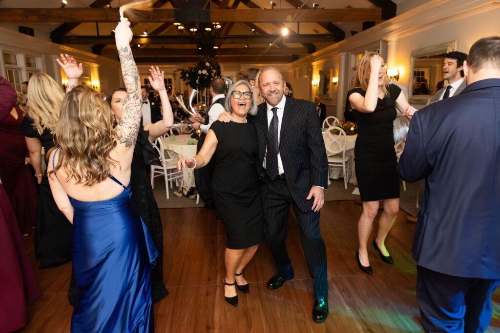 A group of people in formal attire dance and celebrate at an indoor event with wooden floors and decorated tables in the background, highlighting the elegance often found at top wedding venues Atlanta has to offer.