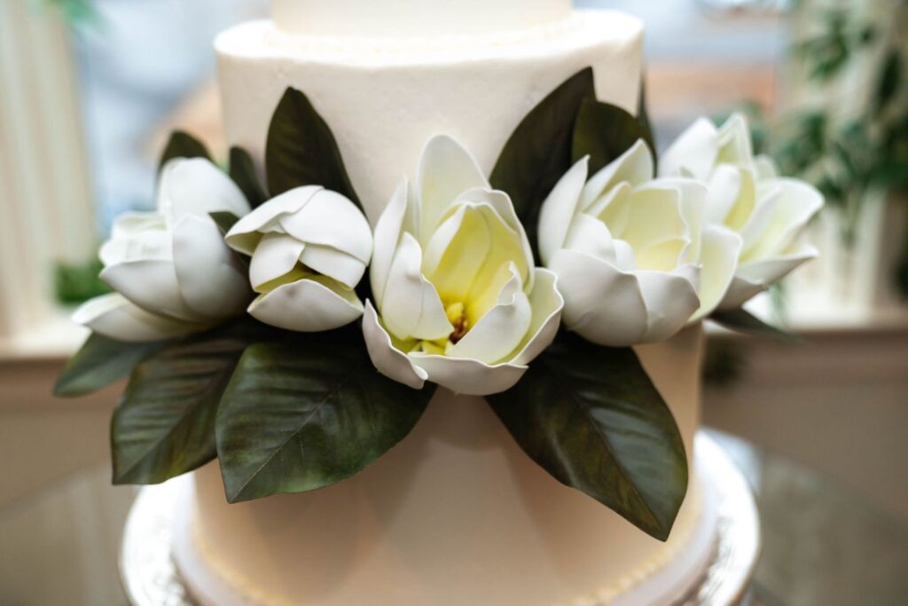 White cake decorated with large, realistic white magnolia flowers and dark green leaves, placed on a glass stand—an elegant centerpiece perfect for wedding venues Atlanta couples adore.