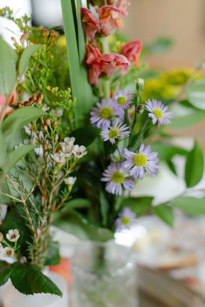 A close-up of a bouquet with purple daisies, white flowers, green leaves, and tall red snapdragons in a clear glass vase—perfect décor inspiration for rehearsal dinner venues Atlanta.