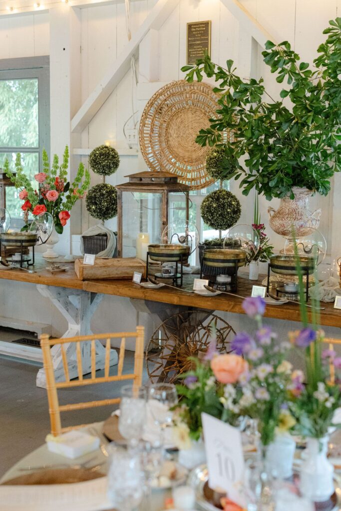 Buffet table with decorative greenery, wicker accents, and chafing dishes. Floral arrangements and candles add elegance—an inviting setup ideal for rehearsal dinner venues Atlanta can offer.