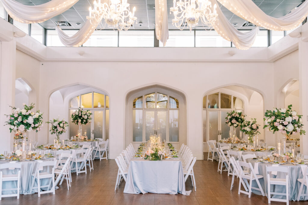 Elegant wedding reception hall with chandeliers, draped fabric, white tables and chairs, floral centerpieces, and candle decorations, set for a formal event and featuring exceptional kosher wedding catering Atlanta couples will love.