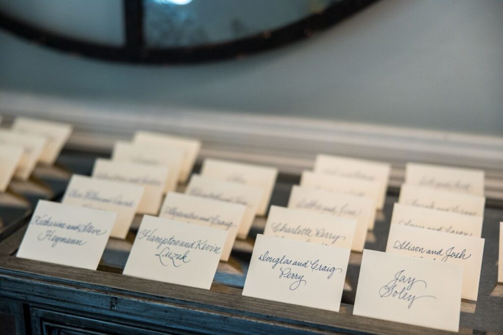 Several handwritten name cards are neatly arranged on a wooden surface, each card displaying a different name in elegant cursive writing, likely for a formal event or gathering such as a wedding or banquet.