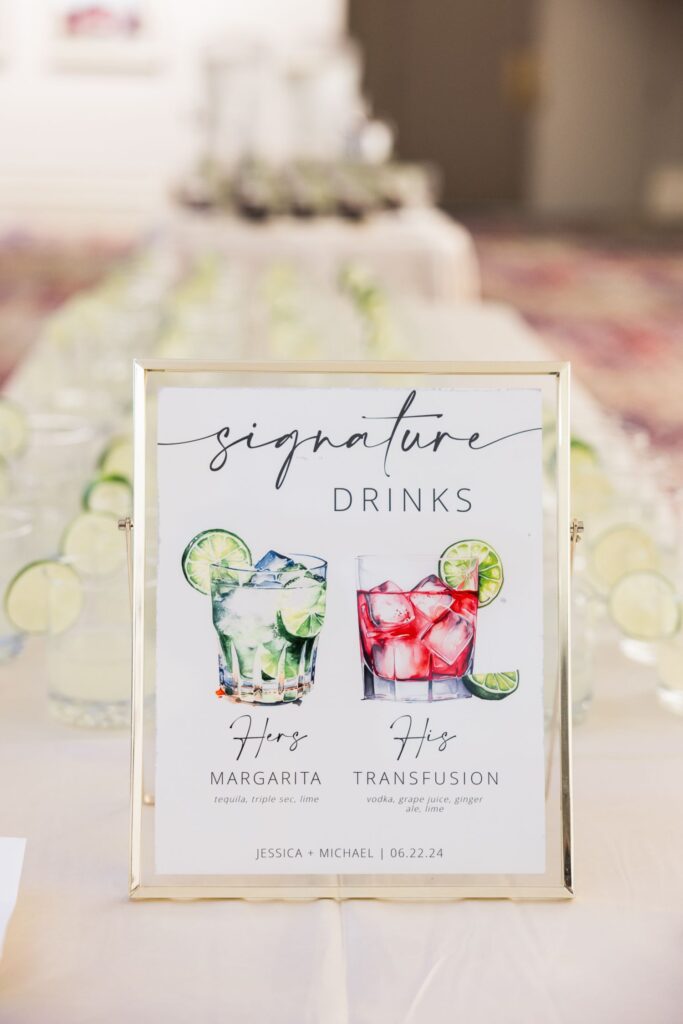 A sign for signature drinks at a kosher wedding reception in Atlanta, featuring illustrations of a margarita labeled Hers and a transfusion labeled His, with the names Jessica and Michael and the date 06.22.24 at the bottom.