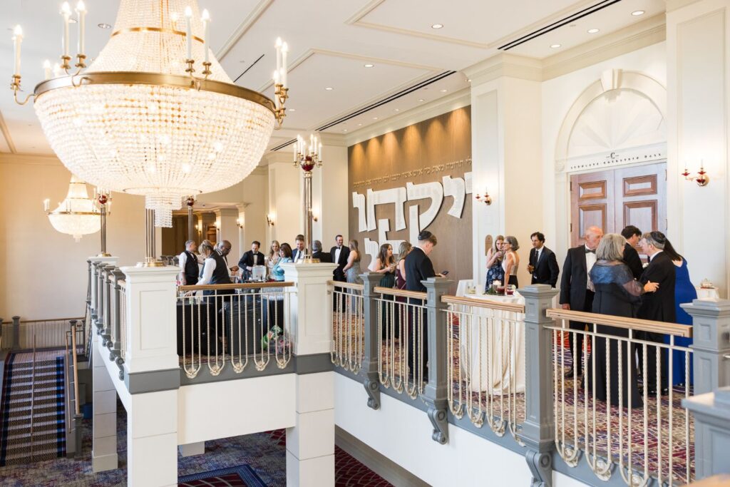 Guests mingle at a kosher wedding reception in Atlanta held in an elegant hall featuring a large crystal chandelier and Hebrew lettering on a feature wall.