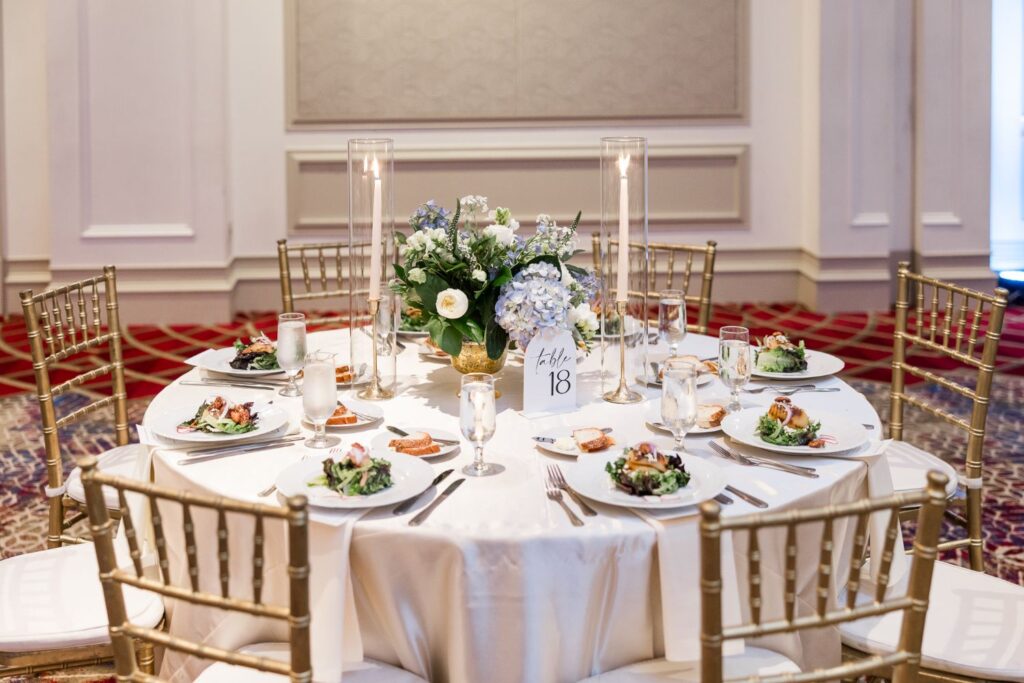 A round dining table set for a formal kosher wedding reception in Atlanta, featuring gold chairs, individual salad plates, tall candles, and a floral centerpiece with a table 18 sign.