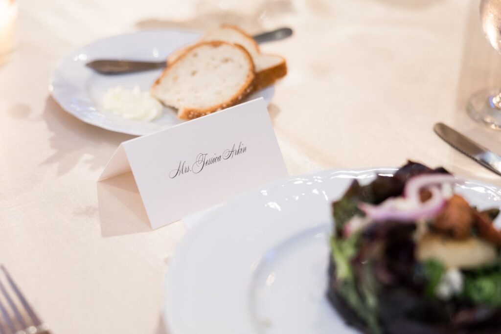 Place card printed with the name Mrs. Jessica Arkin sitting on a table next to a plate of bread and a salad at a kosher wedding reception in Atlanta.