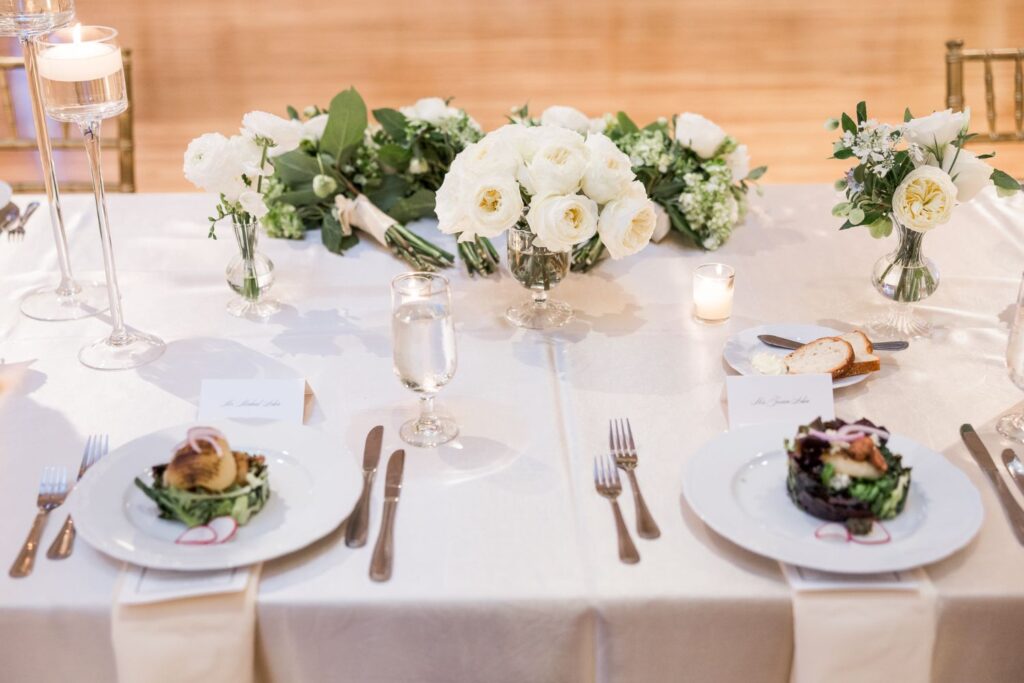 Two place settings at a kosher wedding reception in Atlanta featuring white floral centerpieces, individual plates with salad, and place cards.