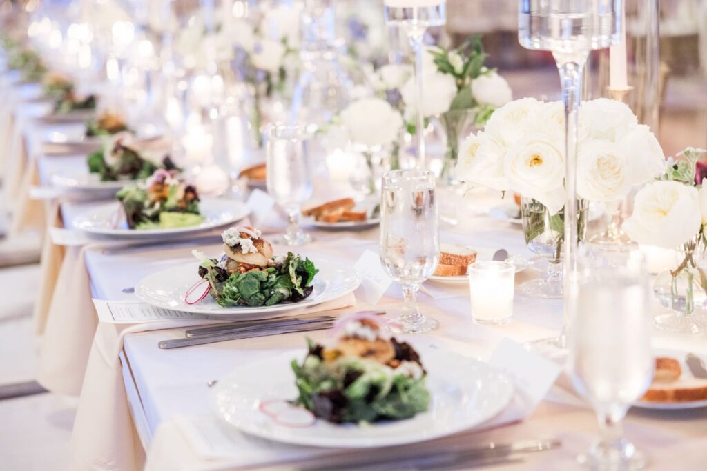A long table set for a formal kosher wedding reception in Atlanta, featuring plated salads, glassware, candles, and white flower centerpieces.