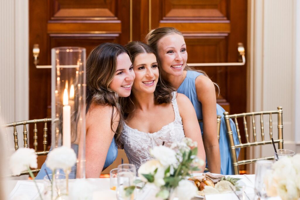 A bride in a white gown smiles while posing with two bridesmaids in blue dresses at an Atlanta kosher wedding reception.