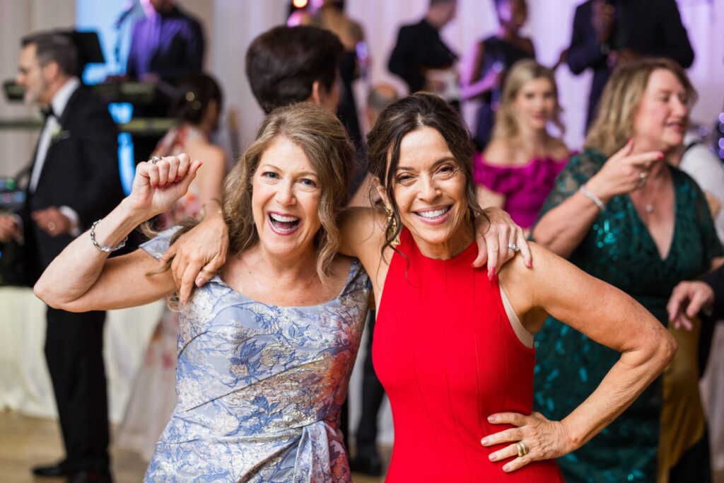 Two women smile and pose with their arms around each other on the dance floor at a kosher wedding reception in Atlanta.