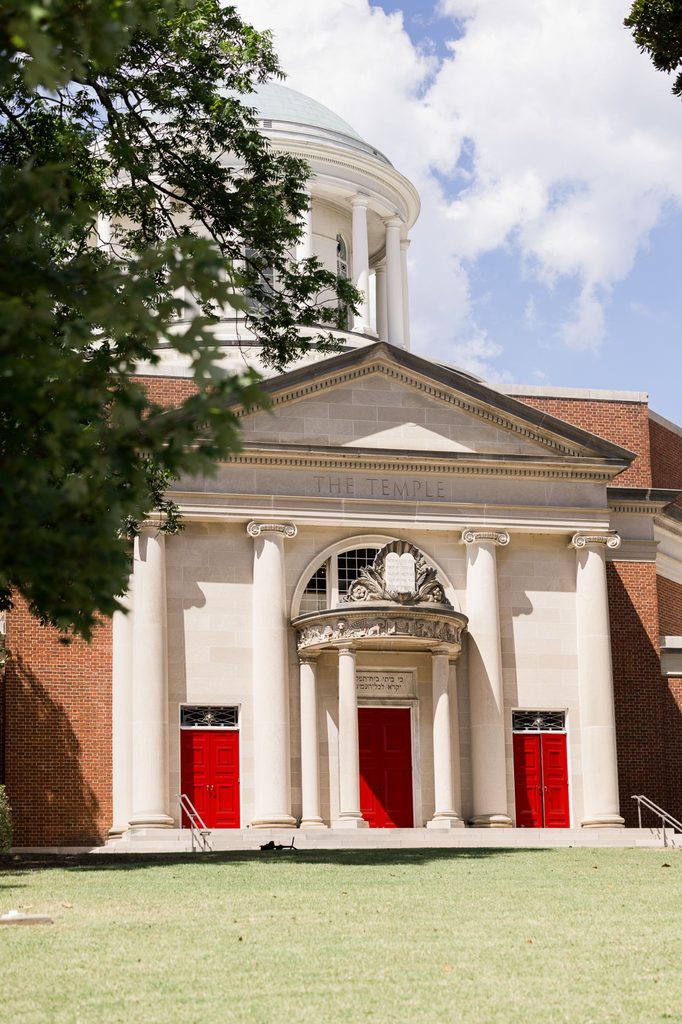 The Temple, a neoclassical building with a central dome, white stone columns, and three vibrant red doors, stands against a green lawn and blue sky, a classic venue for a kosher wedding reception in Atlanta.