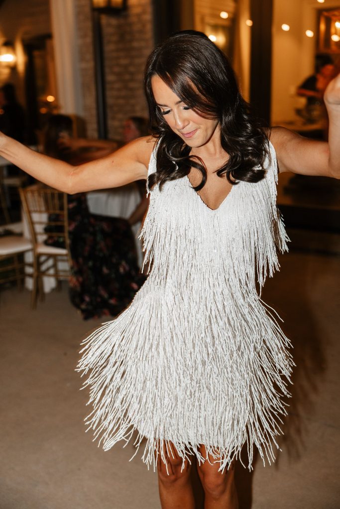 A woman with dark hair dances in a white fringe dress.