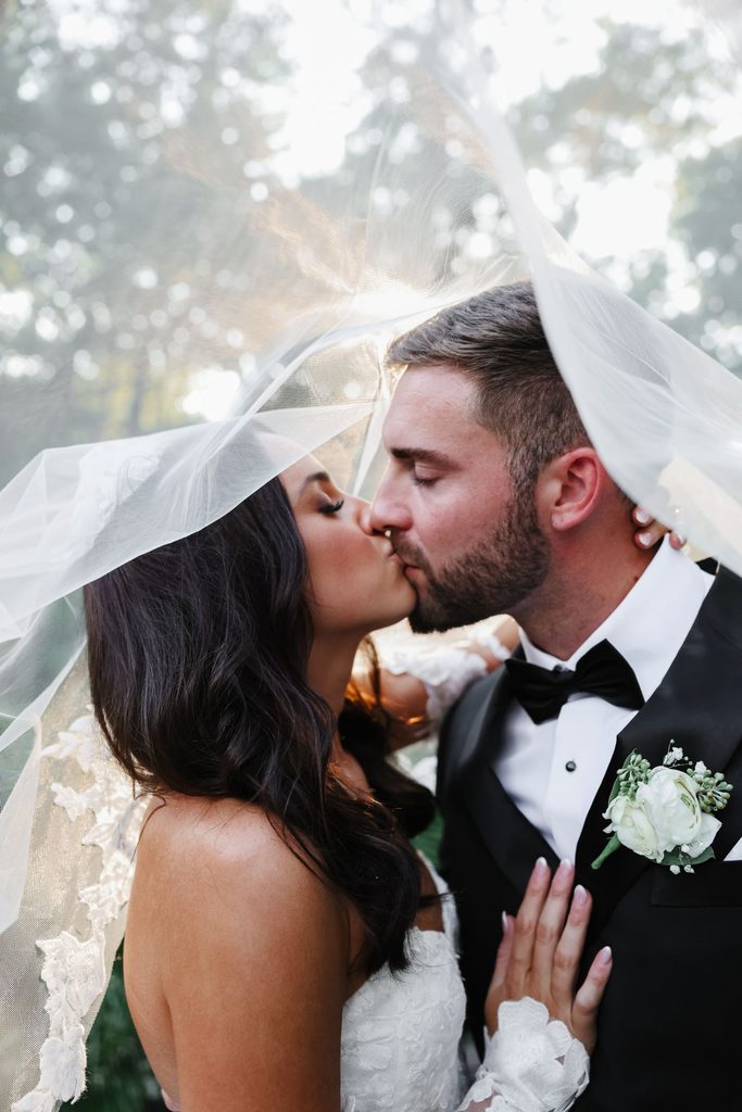 A bride and groom kissing beneath a shared wedding veil.