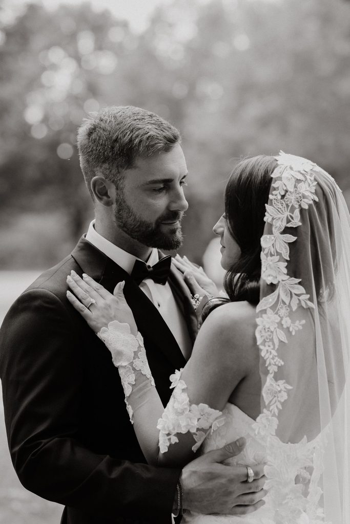 A bride and groom in wedding attire look into each others eyes.