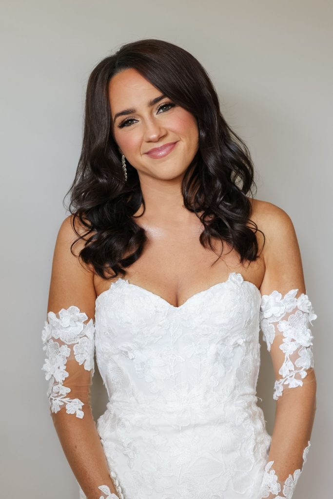 A woman with dark hair wearing a white, strapless, lace-detailed wedding dress.