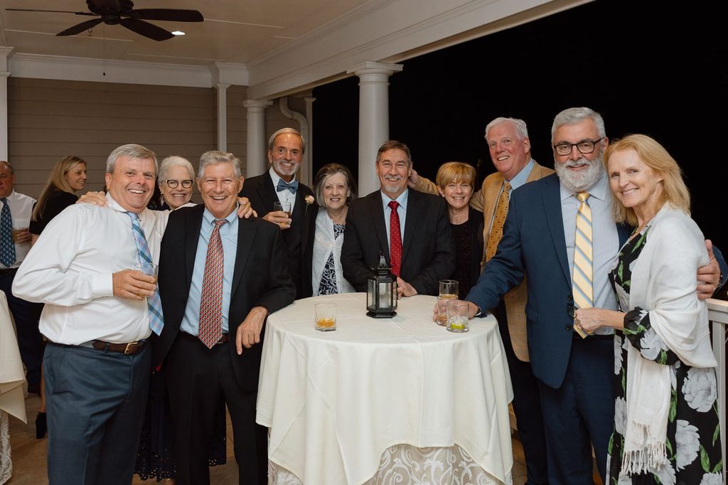 A group of ten adults standing around a circular high-top table at an evening outdoor gathering.