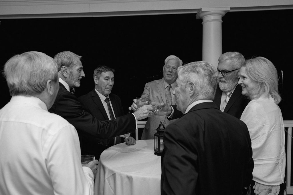 A group of people standing around a circular table at night, clinking glasses for a toast.