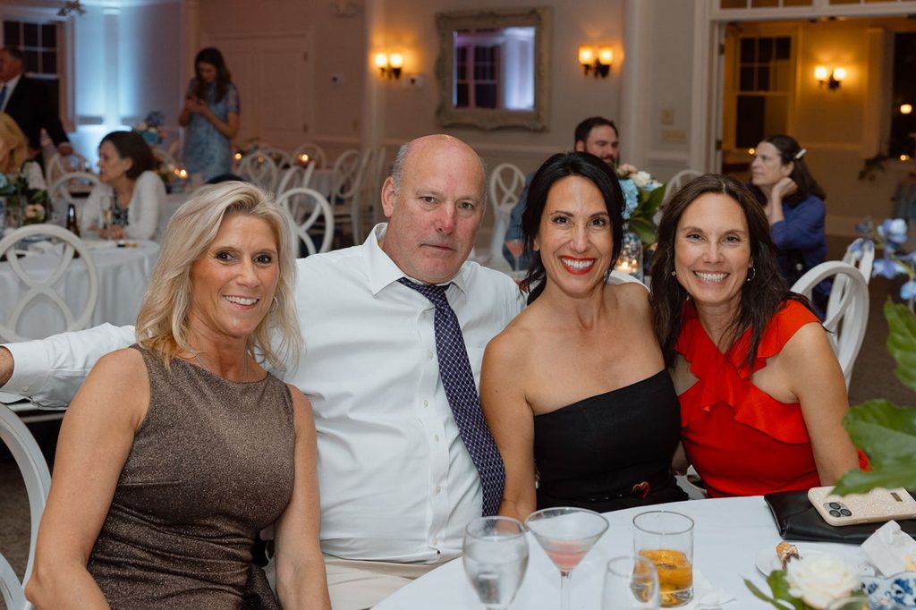 Four people smile while seated together at a dinner table during an event.